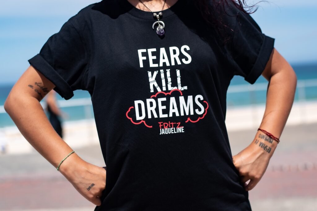 A woman wearing a T-shirt with the inscription "Fears kill dreams" while standing akimbo.