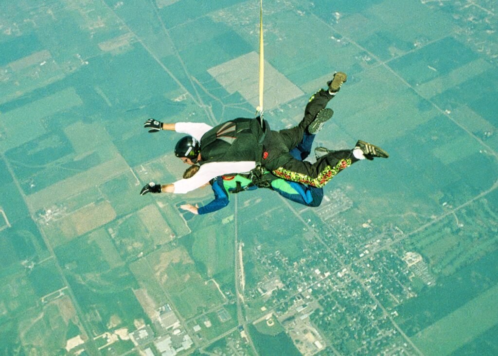 A sky diver and his student diving off a plane with panoramic view of the ground in far sight
