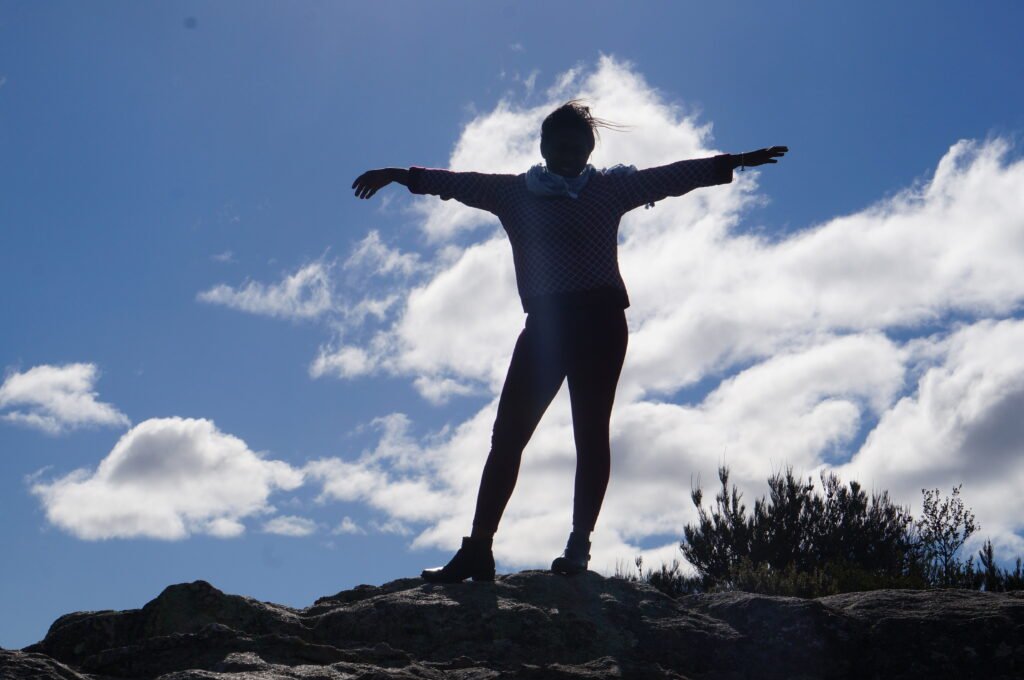 The silhouette of a lady posing with her hands outstretched in the flight posture and a clear blue sky at the background