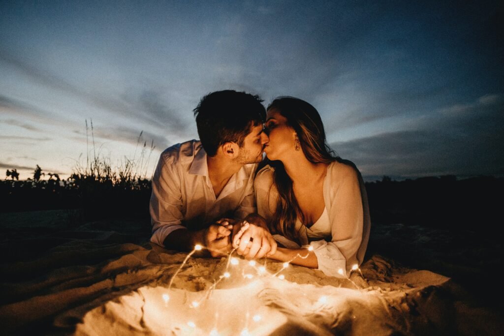 A couple kissing while camping together in the dusk under the moonlight.
