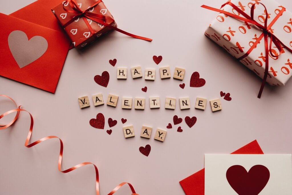 Happy Valentine's Day spelt out with Scrabble tiles surrounded by boxes of gifts, letters and red ribbons