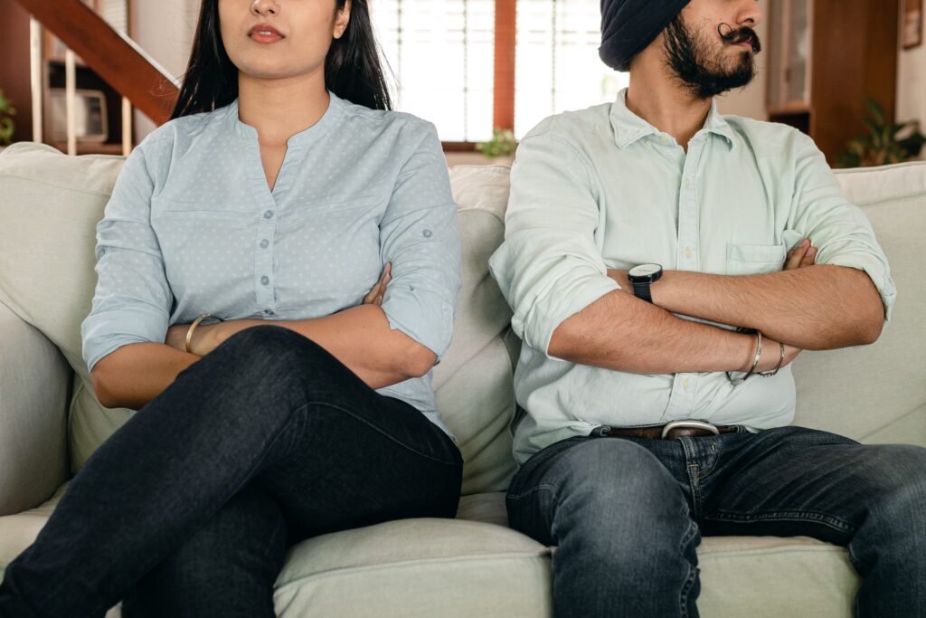 An Indian couple seated uncomfortably on a couch, looking away from each other and with their arms crossed.
