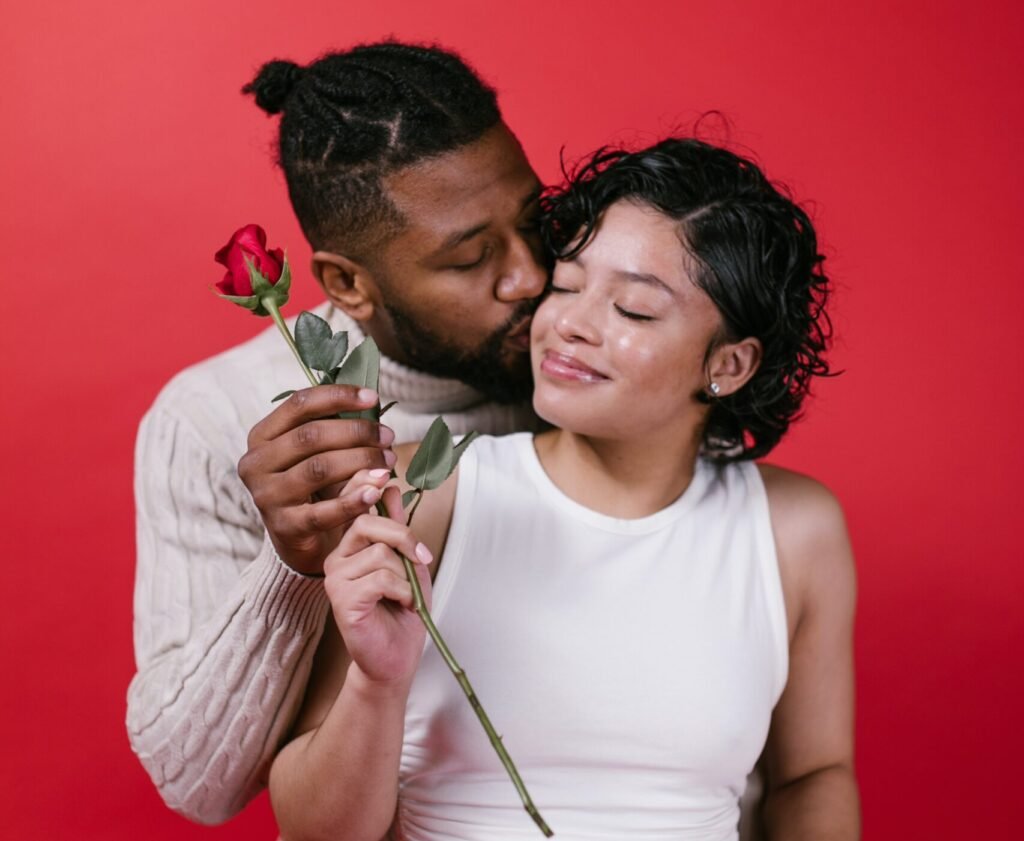 A Black American couple madly in love exchanging a rose and kissing as their preferred Valentine's Day ideas