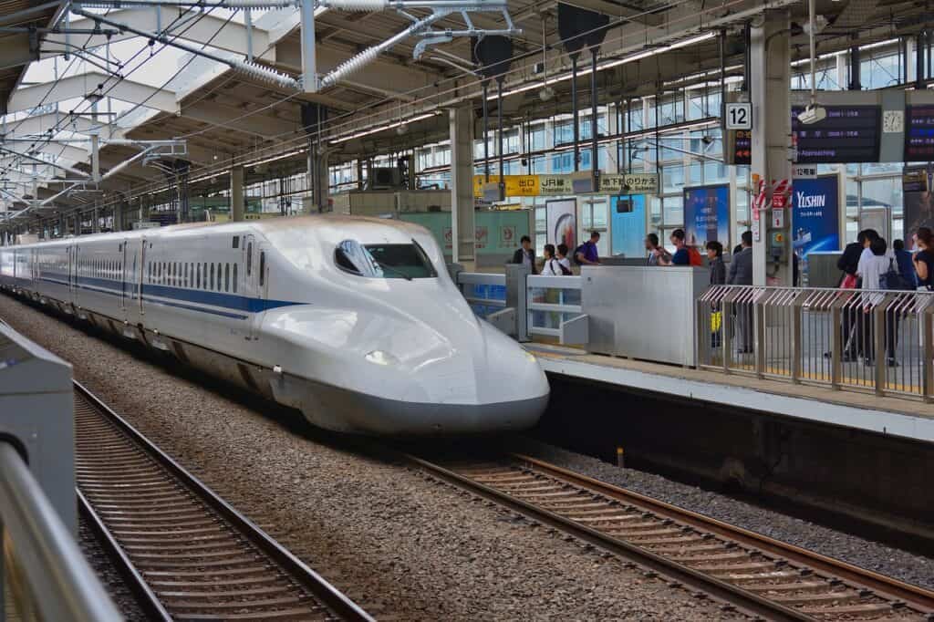 A fast commuter train passing through a station where passengers are waiting to board.