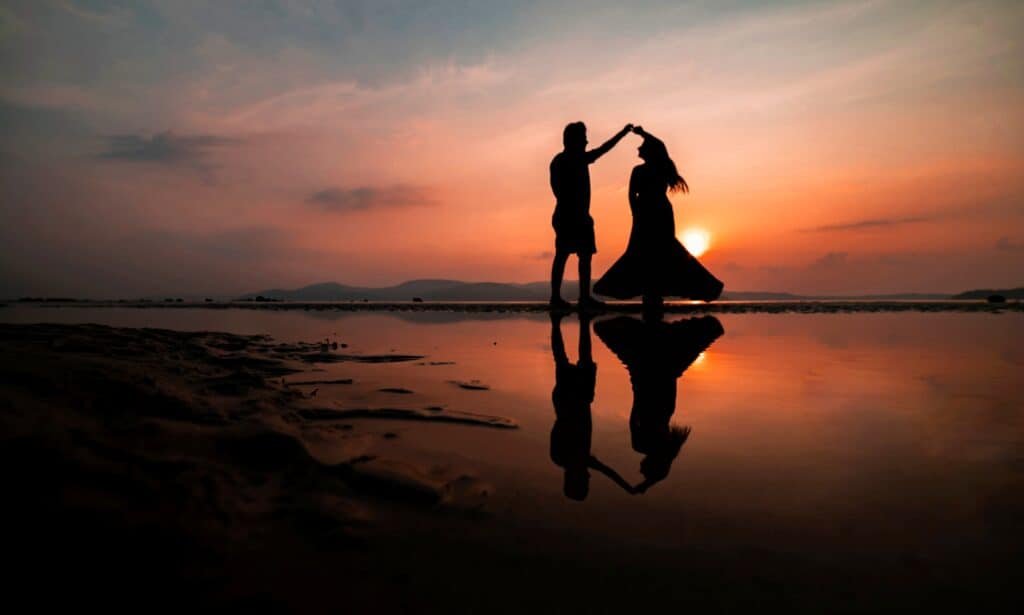 Silhouette of a couple twirling on a beach at sunset.