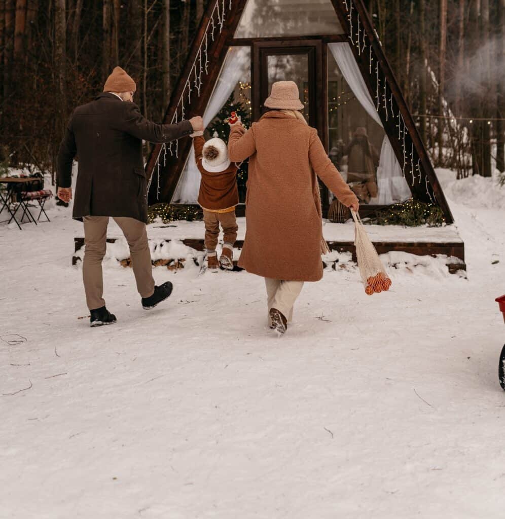 A couple dressed in Winter gear while lifting their little boy up some icy steps to see Santa