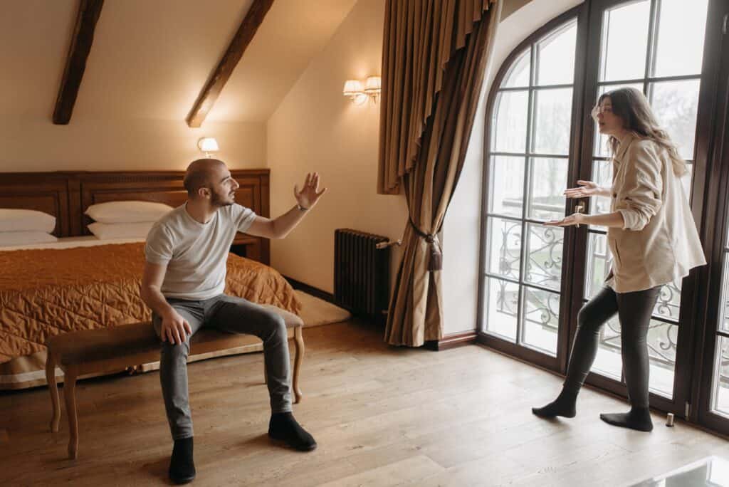 A couple is having heated, loud arguments, with both of them gesturing and the wife close to exiting through the door.