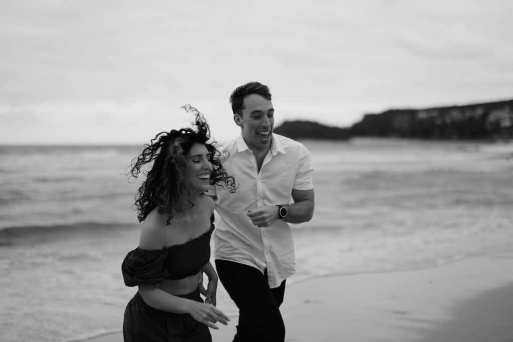A young couple is smiling, and running away from the beach waves