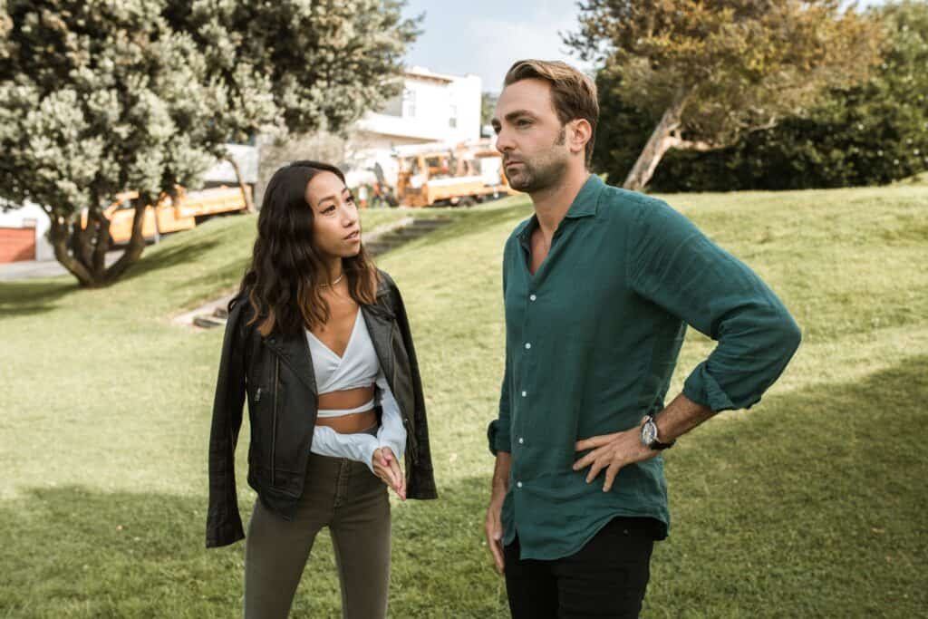 A Black couple engaged in a conversation while standing in their lawn with the wife speaking and the husband listening. 