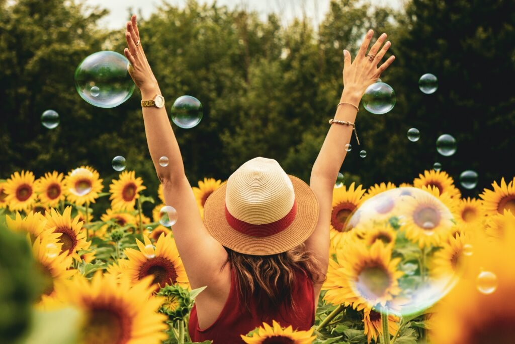 A lady with her arms outstretched inside a Sunflower garden and water bubbles as sign of joy.