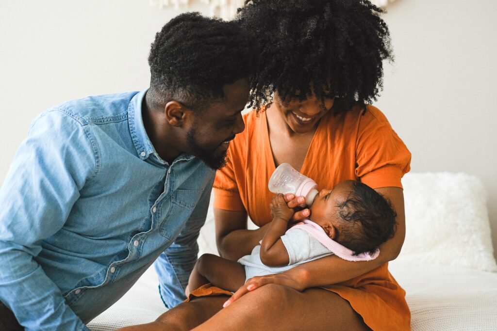 A Black couple happily bottle feeding their new baby in their recent transition to parenthood