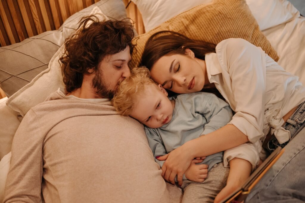 An exhausted couple deep asleep while cuddling their partly awake baby as they struggle to transition to parenthood