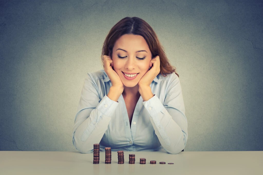 A female executive who is smiling while staring at a pile of coins as evidence she is achieving financial freedom