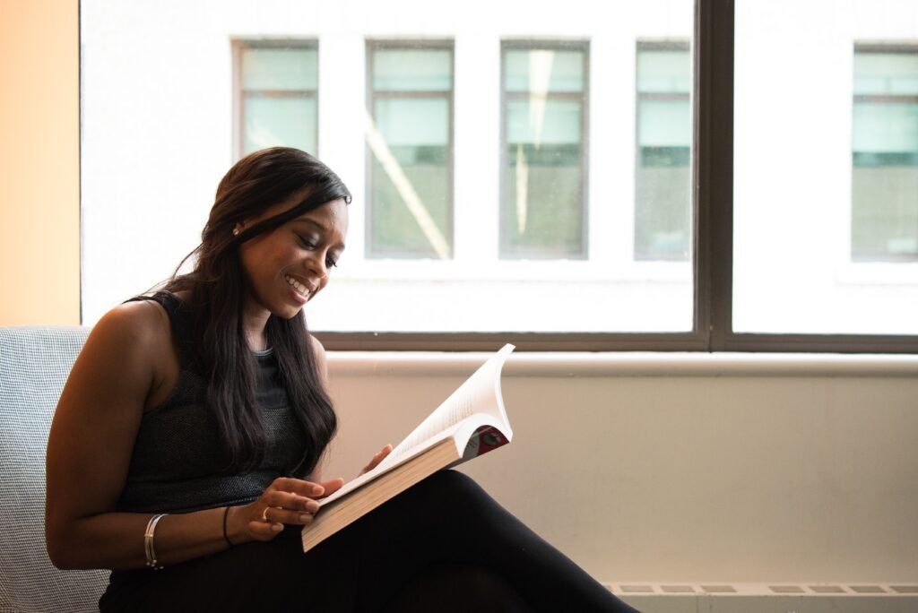 A Black lady smiling while reading a great book in her lounge.