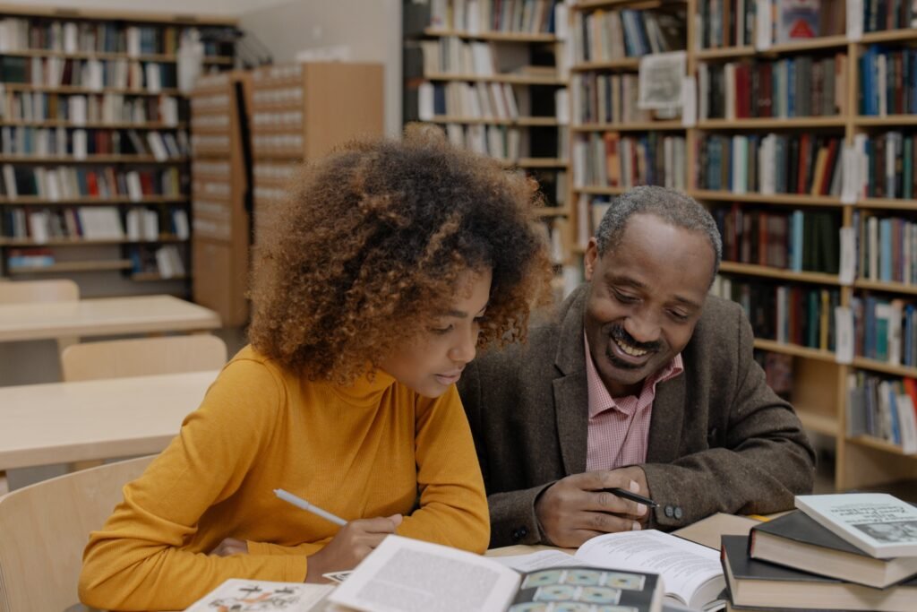 An African man with his daughter in the library, sharing ideas from a book on personal growth and development