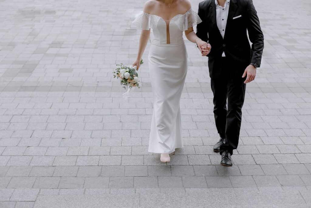 A young couple marching hand in hand on their wedding day. They appear unaware of the relationship myths they may face in future.