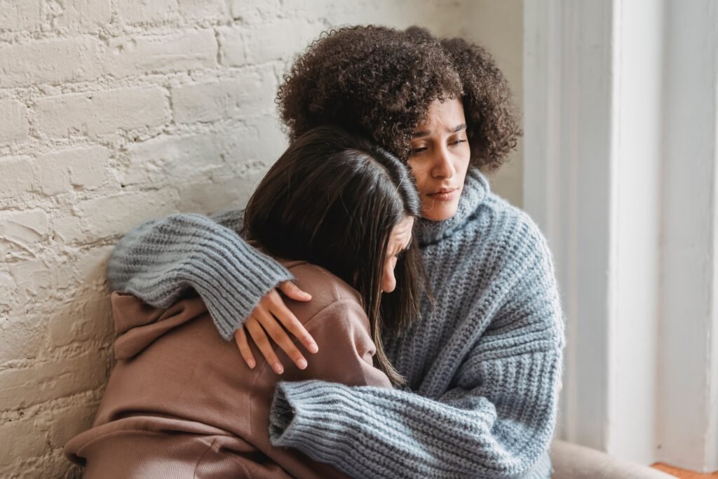 Two Black American sisters are leaning on each other's shoulders as they mourn a family member's loss.