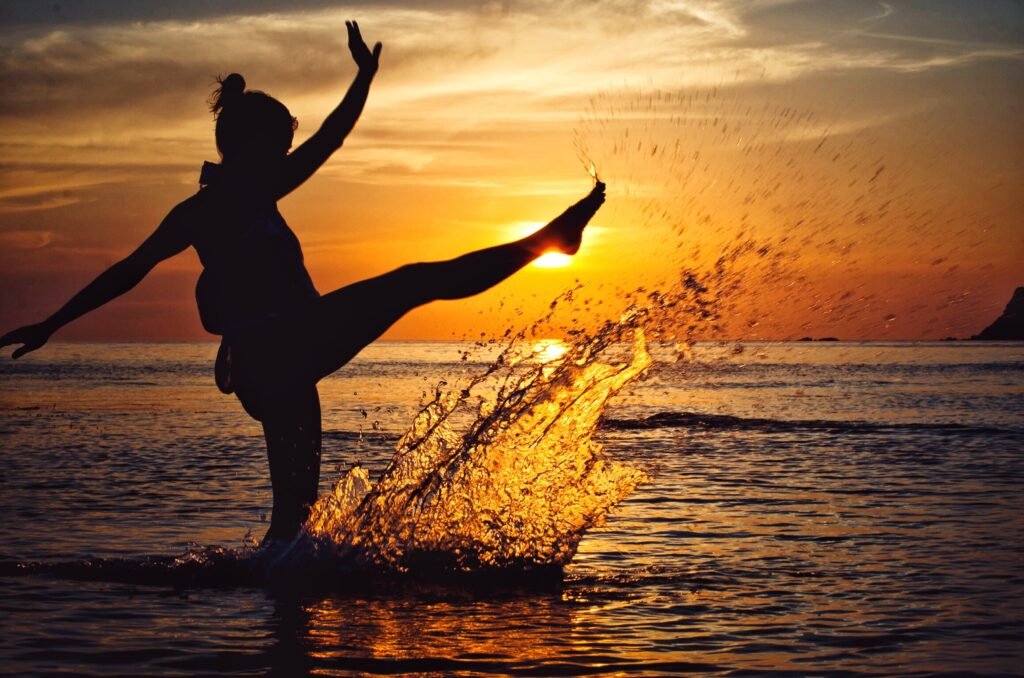 A lady is silhouetted on the sunrise while kicking water in the beach after learning how to cope with tough times.
