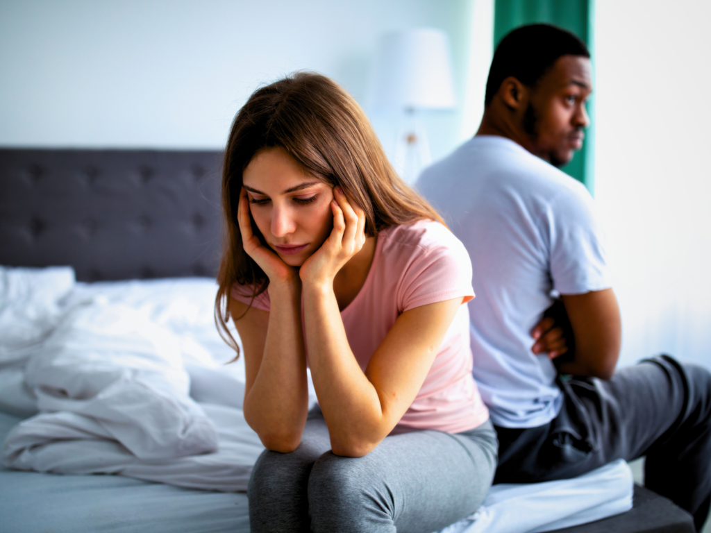 A couple backing themselves while seated on bed looking. The wife is looking sad and resentful of her cheating husband.